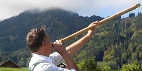 Mann bläst in ein Alphorn in den Bergen