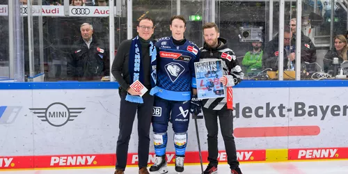 Drei Menschen auf einer Eisfläche in einem Stadion, zwei Sponsorenpartner überreichen einem Eishockeyspieler einen Award