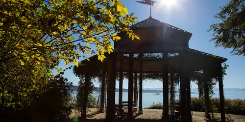 Blick auf einen See bei dem im Vordergrund ein schönes hölzernes Pavillon steht, die Sonne scheint