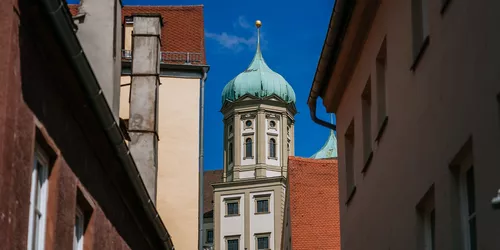 Blick durch eine enge Gasse hindurch auf eine Kirche, man sieht vor allem den Kirchturm