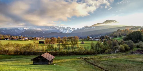 Blick auf eine Voralpenwiesenlandschaft mit Scheunen und Bergpanorama im Hintergrund