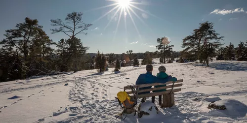 Verschneite Winterlandschaft mit einem Paar auf einer Sitzbank am Altmuehltal Panoramaweg